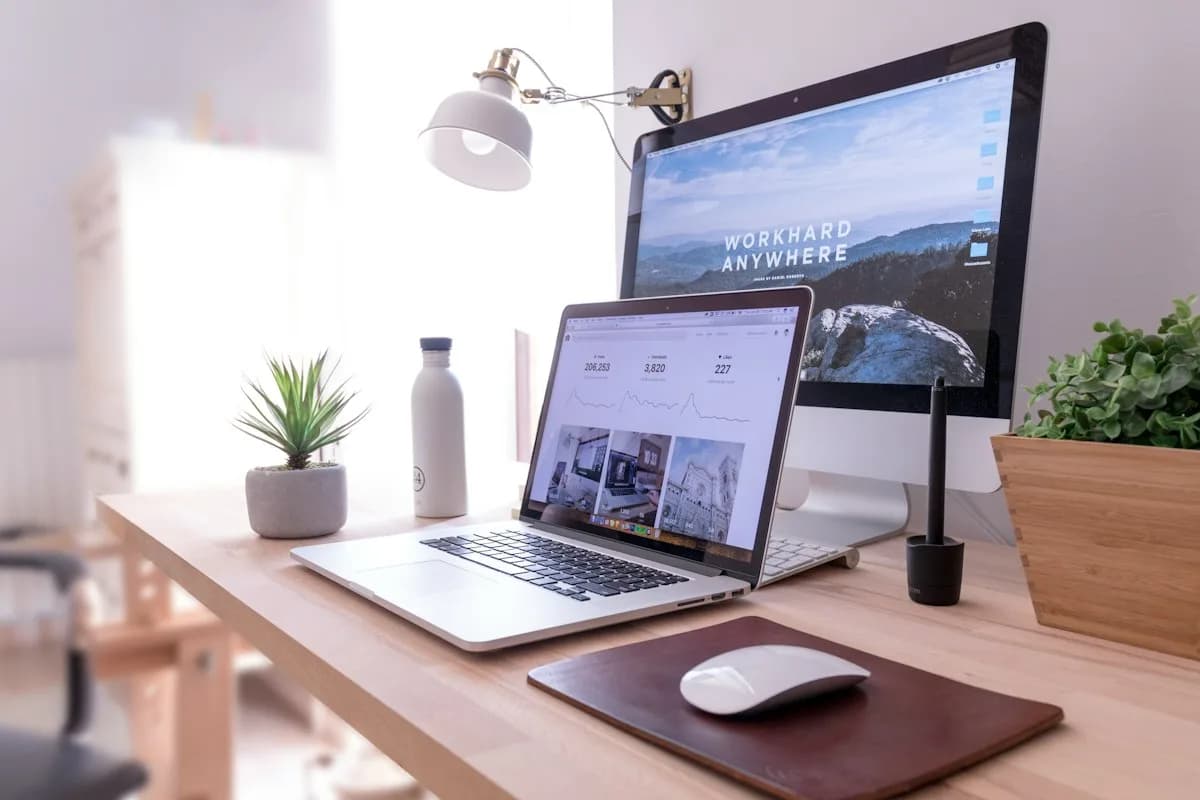 A laptop and desktop computer on a tidy desk with plants